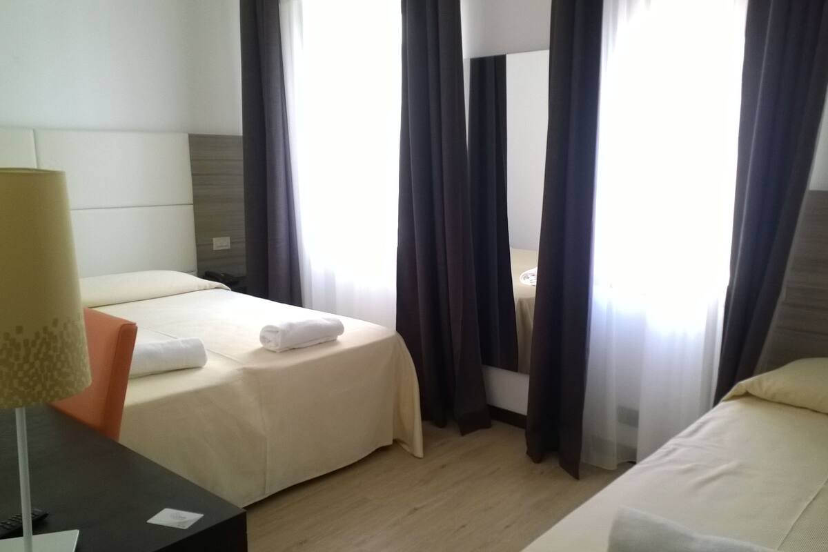 Habitación de hotel con dos camas, un escritorio y una lámpara.