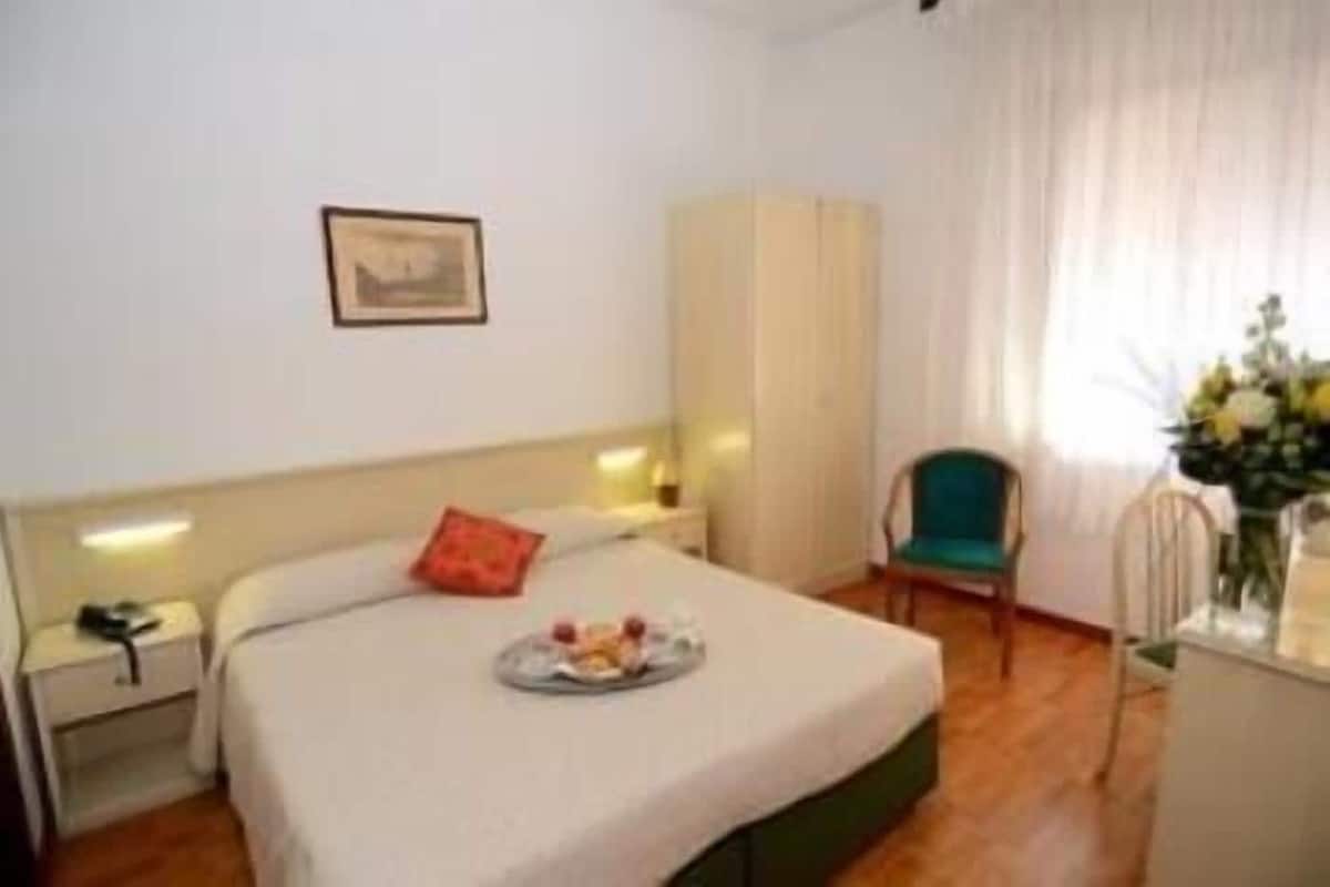 Una habitación de hotel con una cama, una silla, un escritorio y un cuadro en la pared.