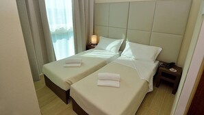 Une chambre d’hôtel avec deux lits simples, une table de chevet avec une lampe et une fenêtre avec des rideaux.