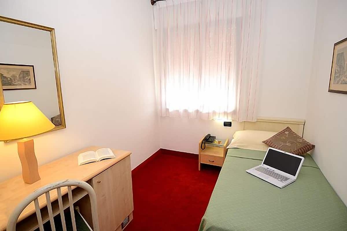 Un dormitorio pequeño y ordenado, con escritorio, cama, silla y ventana con cortinas.