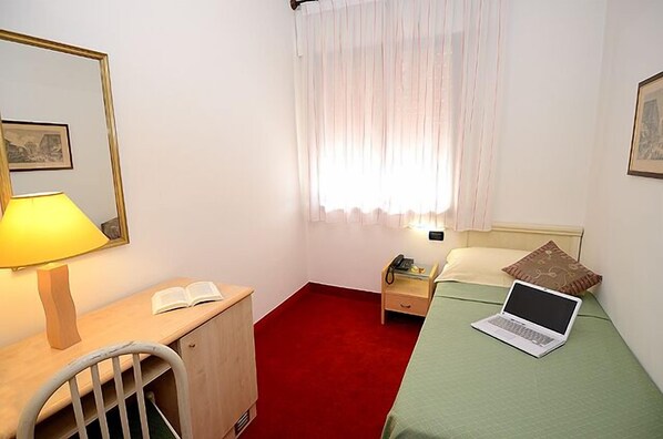 A small, neatly arranged bedroom with a desk, a bed, a chair, and a window with curtains.