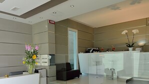 Un espace d’accueil moderne avec un bureau blanc, un vase de fleurs et une cloison en verre.
