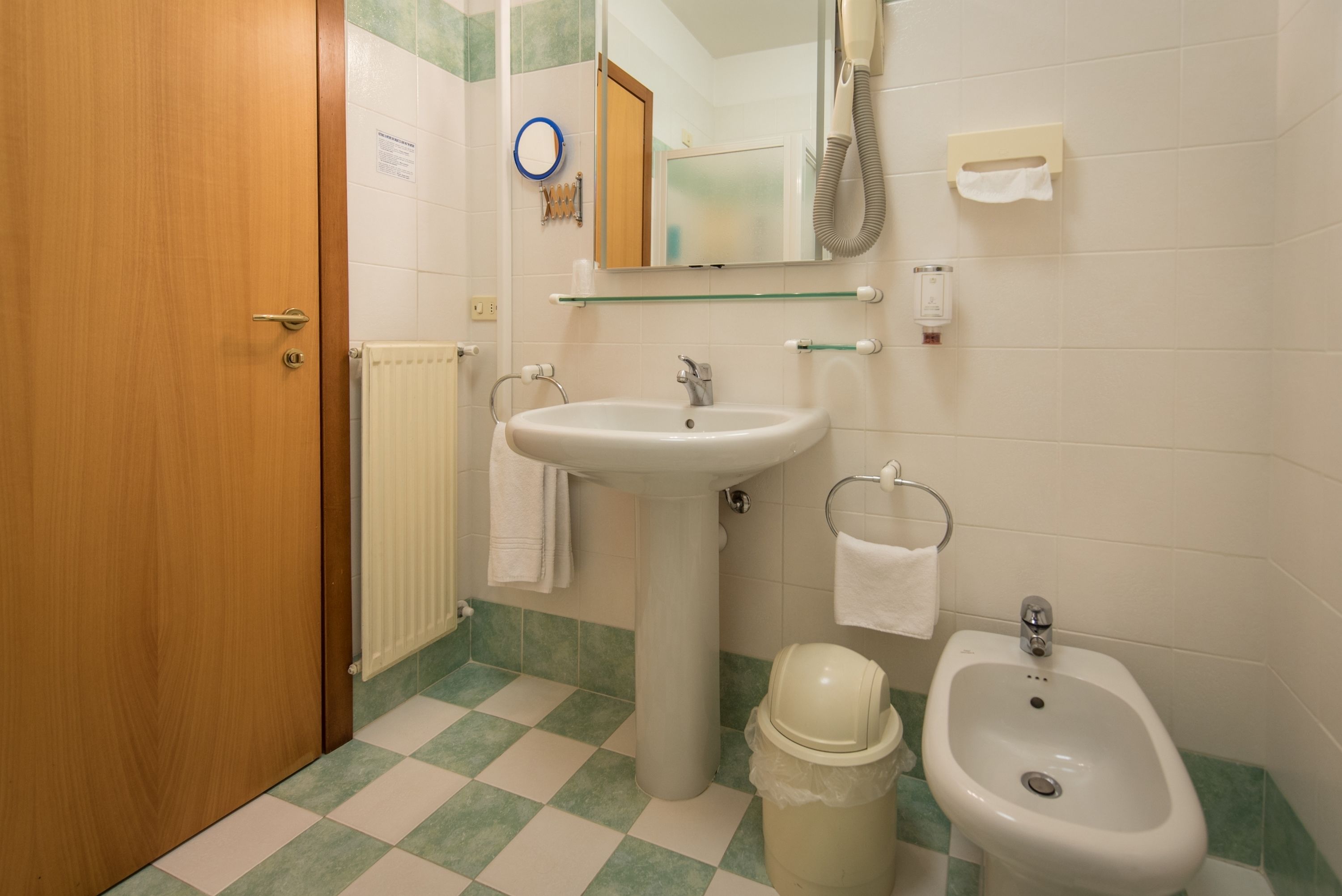 A bathroom with a wooden door, a white sink, a bidet, and a mirror.