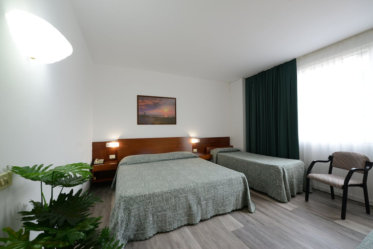 A hotel room with two beds, a chair, a nightstand, a lamp, and a painting on the wall.