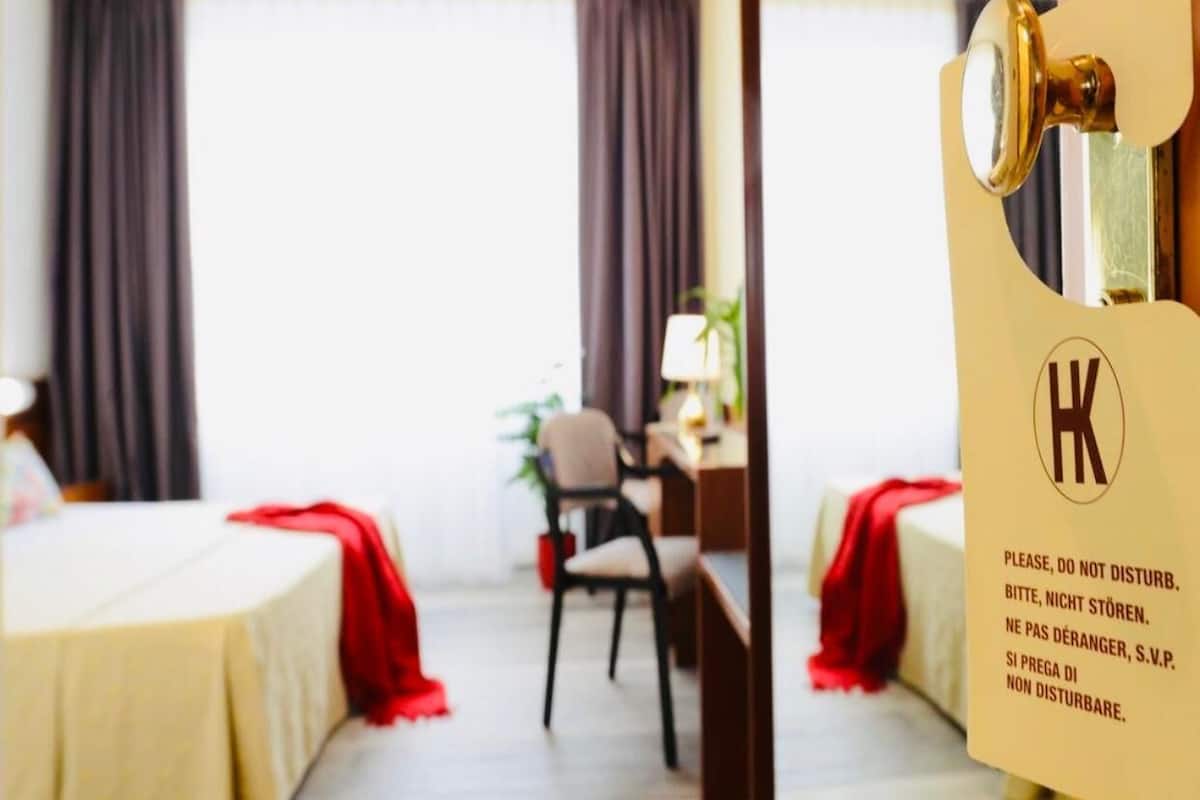 A hotel room with a bed, a desk, a chair, and a window with curtains.