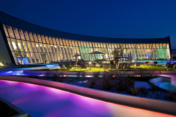 A modern hotel with a curved glass facade, outdoor seating area, and a pool. - Hotel Krystal (Bussolengo)