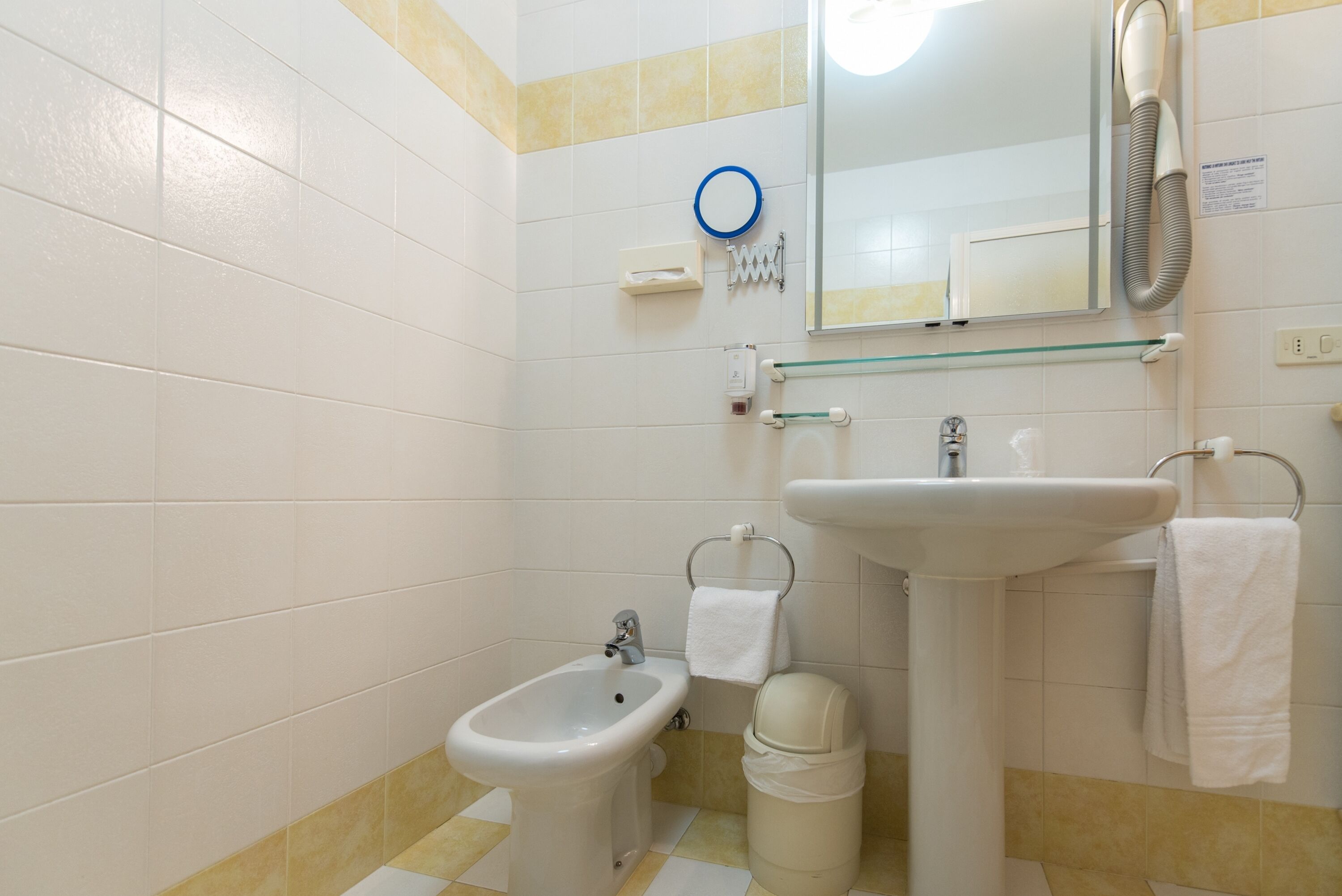 Un baño con bidé, lavabo, espejo, toallero y un cubo de basura.