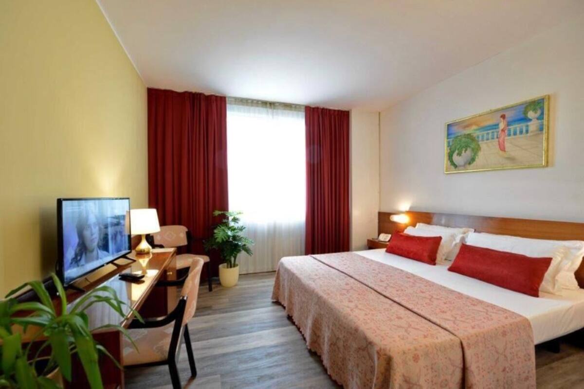 A hotel room with a bed, a desk with a television, a lamp, and a painting on the wall.