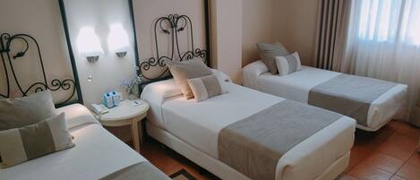 Habitación de hotel con dos camas individuales, una mesita de noche redonda con lámpara, teléfono y un jarrón con flores.