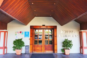 La entrada del Hotel Alboran, con fachada de madera, puertas dobles y dos plantas en macetas.