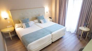 Una cama doble con cabecera, dos mesitas de noche, una lámpara, un teléfono y una pequeña mesa redonda con un florero.