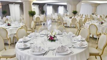 A banquet hall with round tables set for a formal event, featuring white tablecloths, gold chairs, and floral centerpieces.