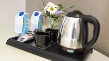 A tray with a coffee maker, two milk cartons, a vase with flowers, and a packet of coffee creamer.