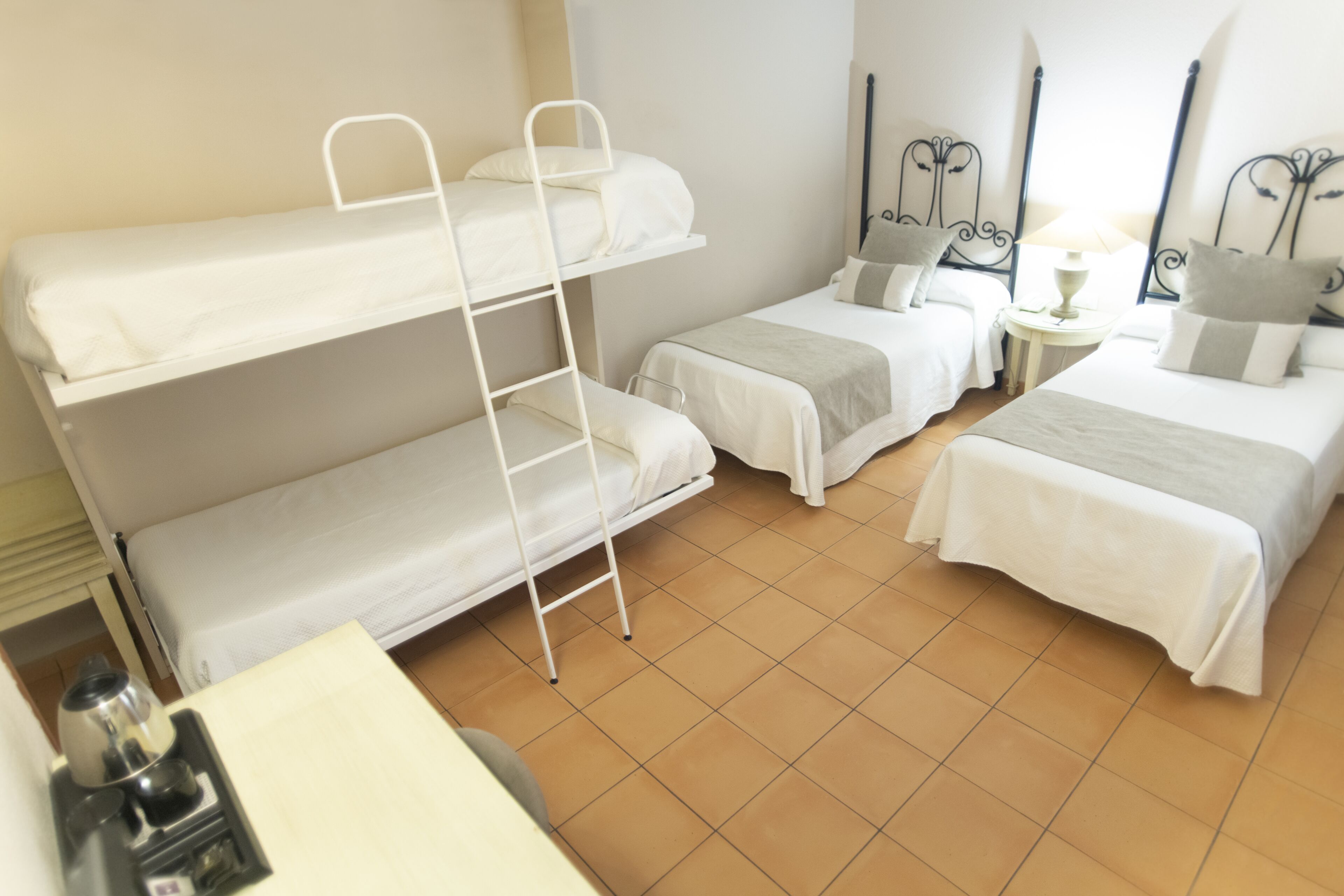 A room with bunk beds, a desk, and a nightstand with a lamp.