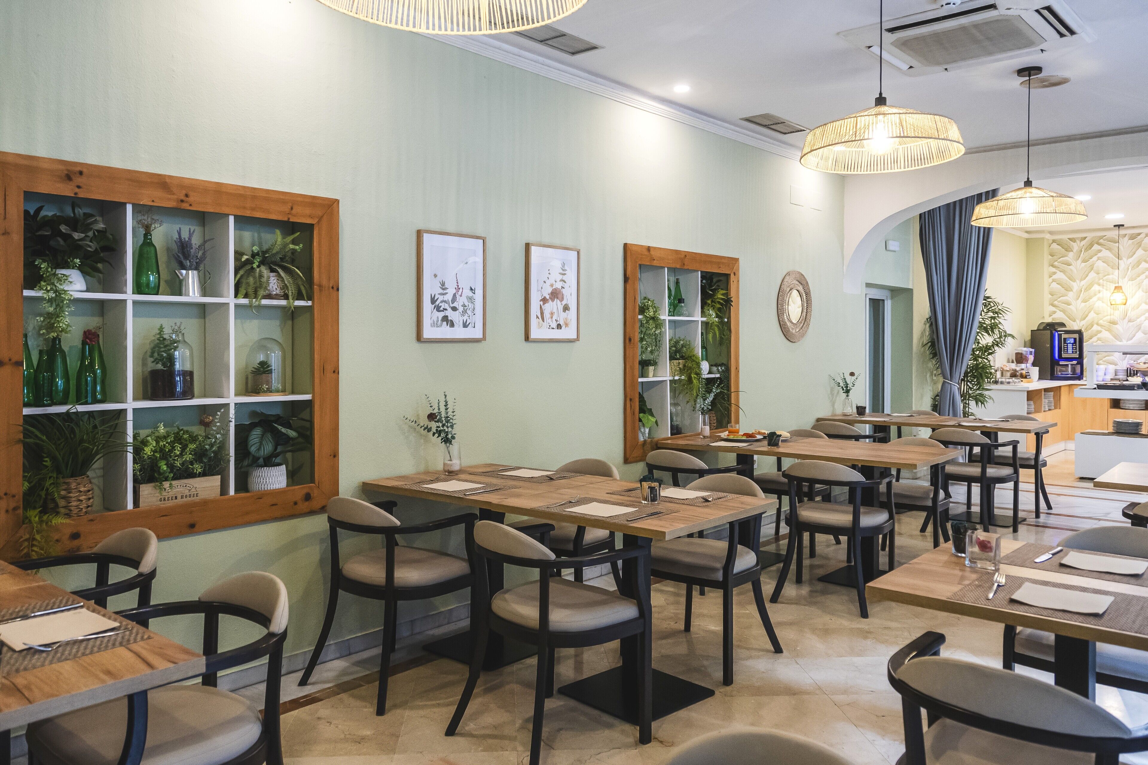 Interior de un restaurante con varias mesas y sillas, vigas de madera y plantas verdes en los escaparates.