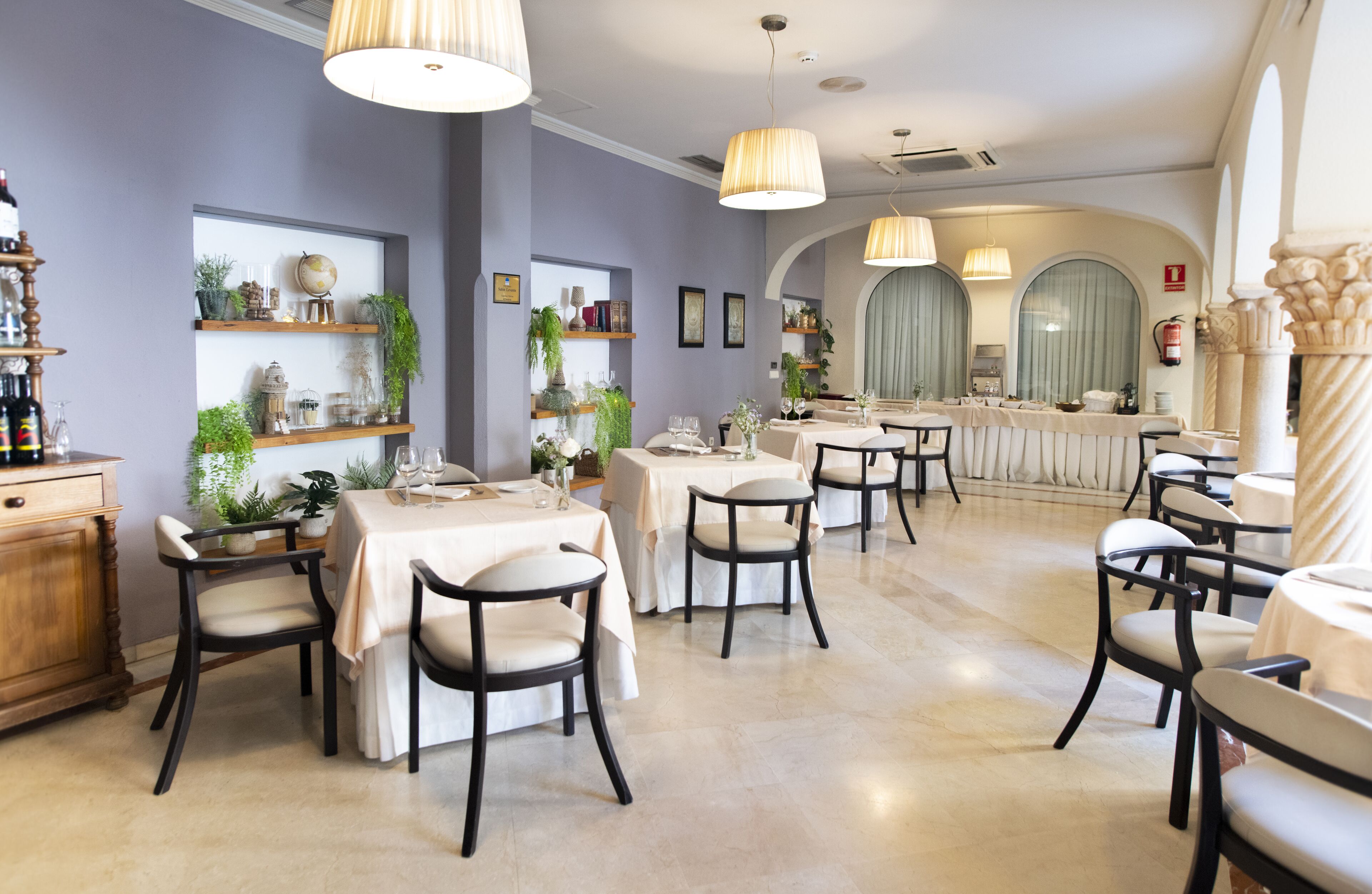 Un comedor con mesas y sillas, estanterías con plantas y una zona de bar con mostrador.