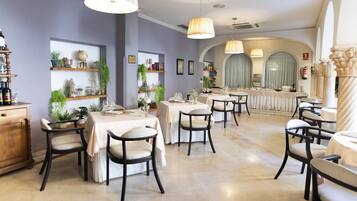 Un comedor con mesas y sillas, estanterías con plantas y una zona de bar con mostrador.