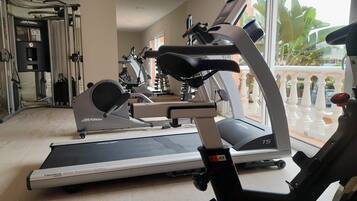 Une salle de sport à domicile équipée d’un tapis de course, d’un vélo elliptique et d’appareils de musculation.