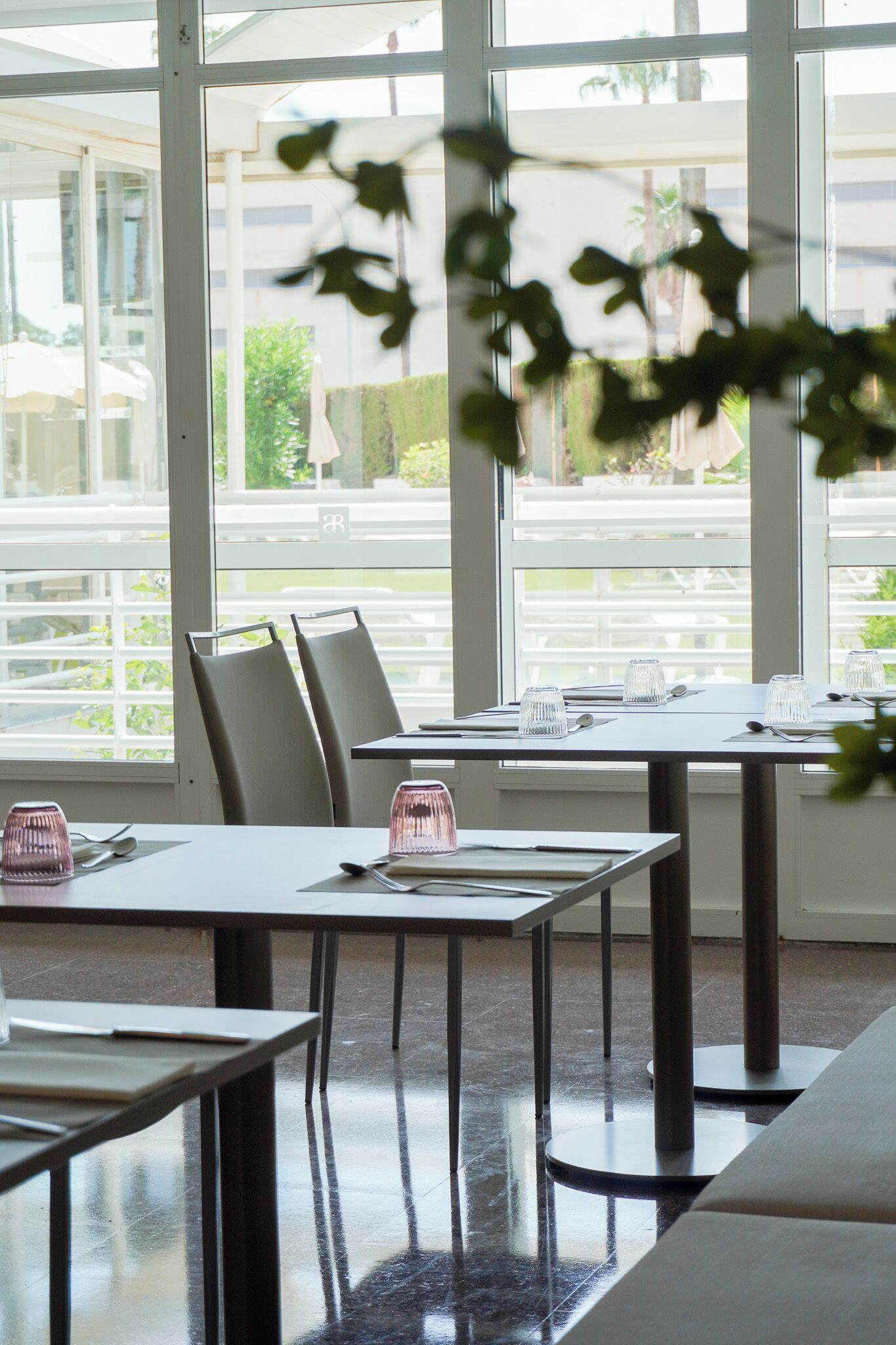 Un restaurante con mesas y sillas, ventanas amplias y vistas a zonas verdes.