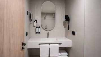 A modern bathroom with a white sink, a large mirror, and a hairdryer mounted on the wall.