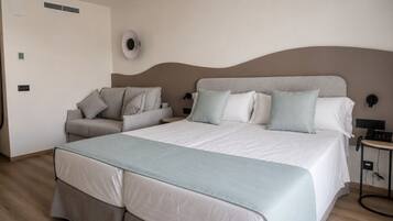 A hotel room with a bed, a sofa, a bedside table, and a wall-mounted lamp.