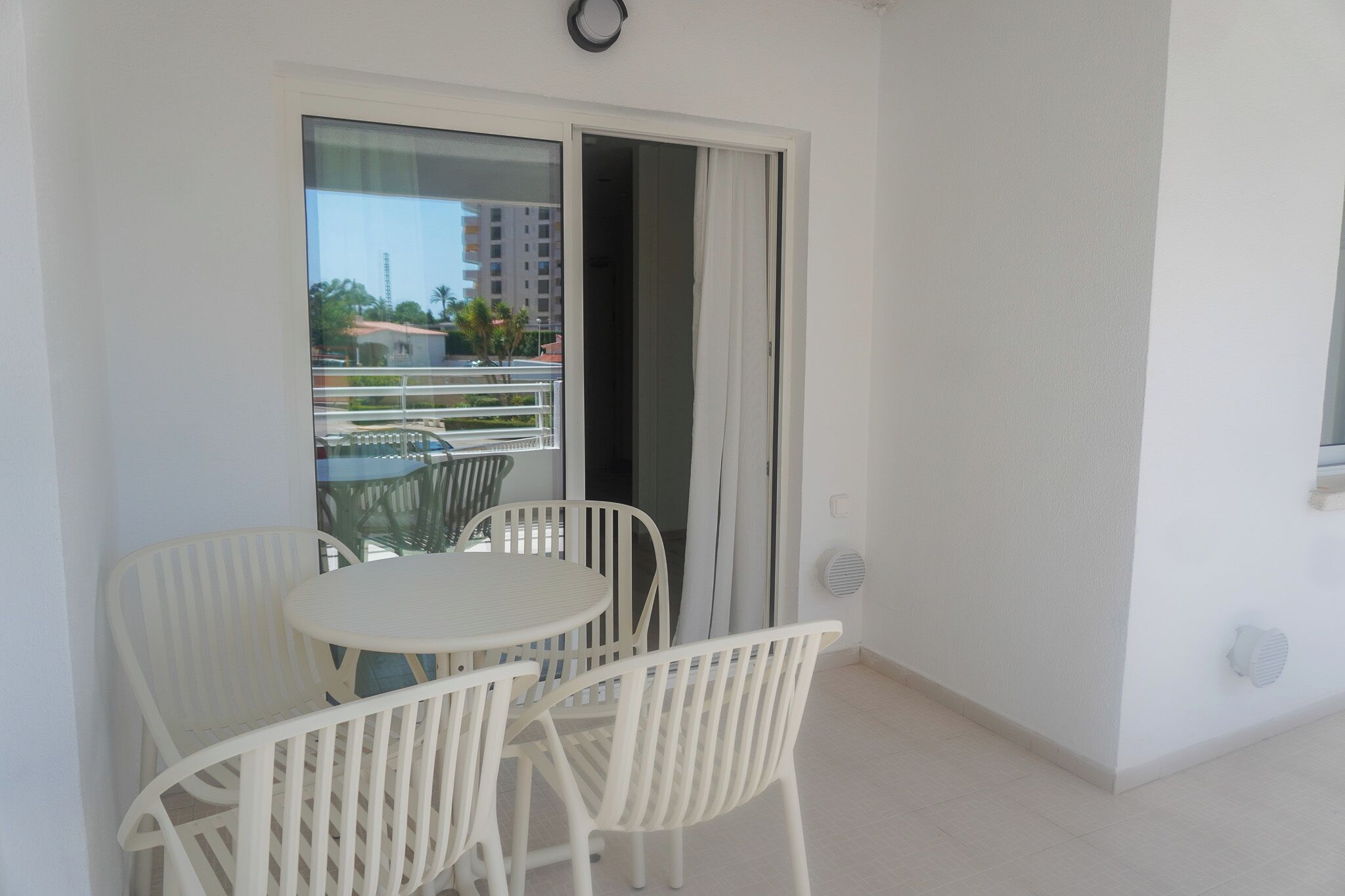 Een balkon met een tafel, stoelen, een schuifpui en uitzicht op gebouwen en palmbomen.
