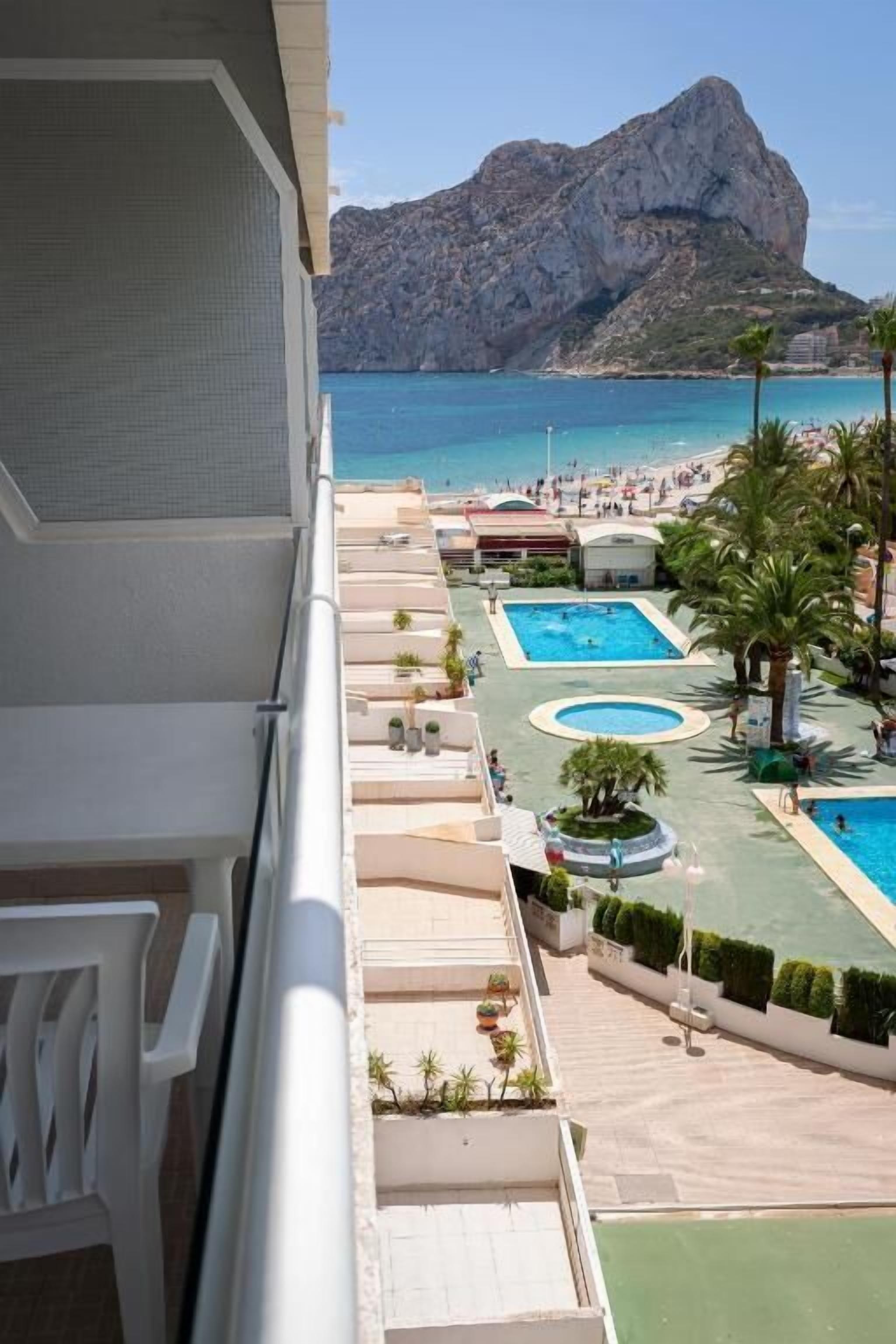 A hotel balcony with a view of a beach, a pool area, and a mountain in the background.