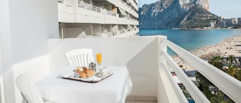 Ein Balkon mit Frühstückstisch, mit Blick auf Strand und Berge.