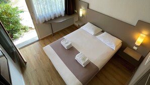 Une chambre d’hôtel avec un grand lit, deux tables de chevet, une fenêtre avec des rideaux et une vue sur la verdure.