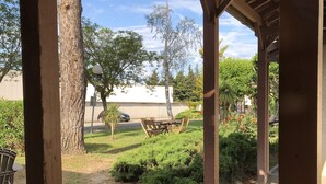 Un espace extérieur abrité, doté d’une pergola en bois, d’une table de pique-nique et d’une pelouse avec un petit arbre et des arbustes.