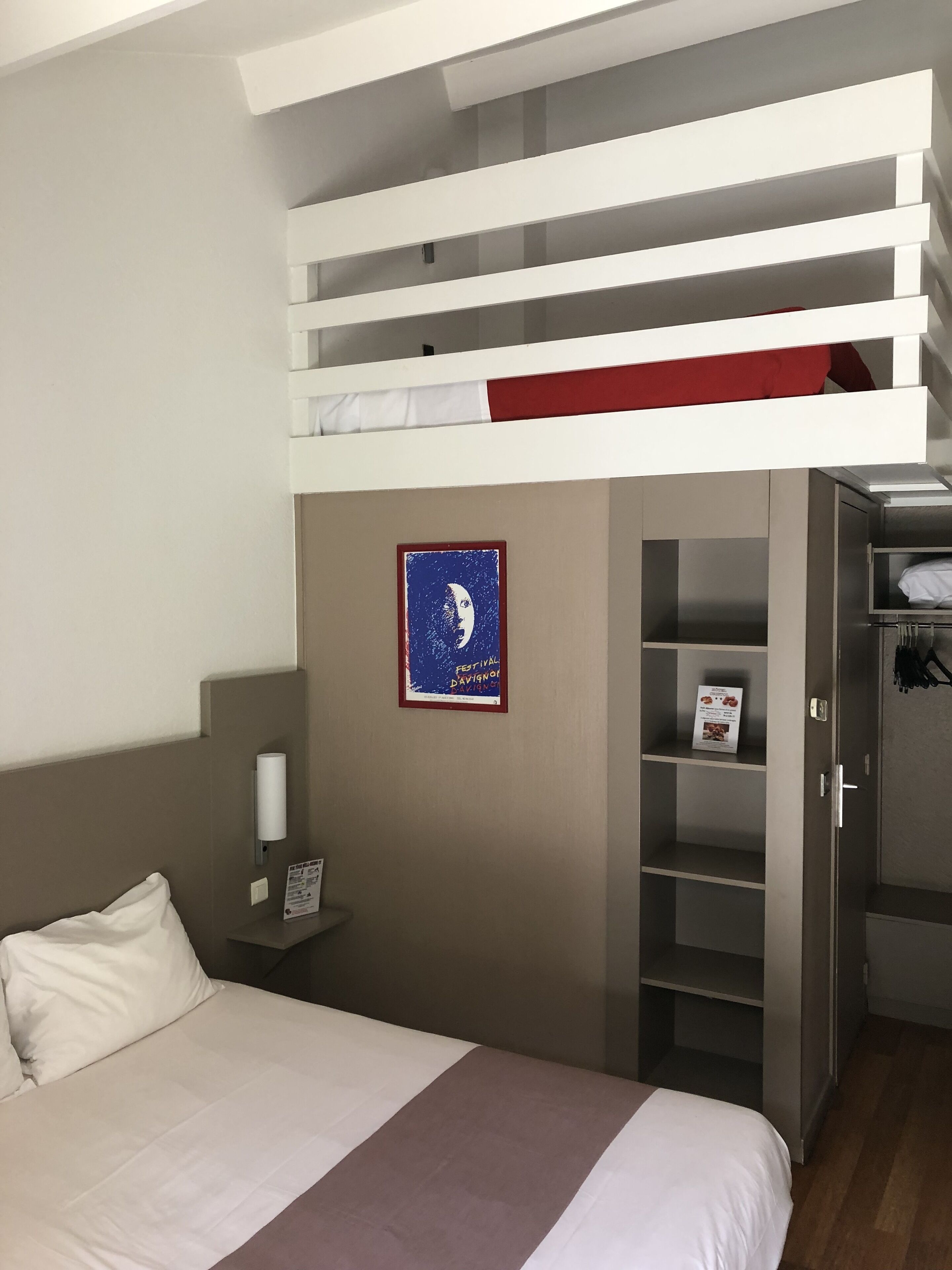 A hotel room with a bunk bed, a bed, a nightstand, a wardrobe, and a poster on the wall.