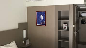 A hotel room with a bunk bed, a bed, a nightstand, a wardrobe, and a poster on the wall.