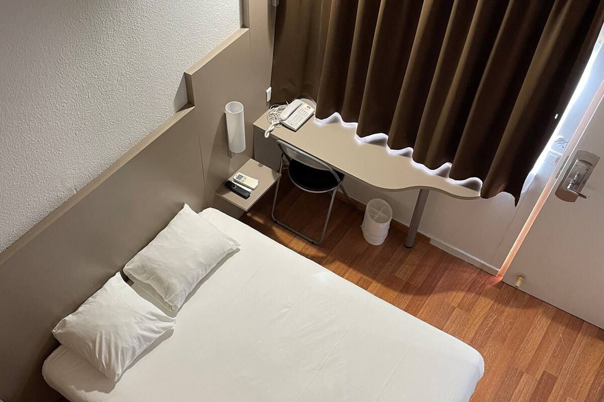 A hotel room with a bed, a desk with a telephone, and a chair.