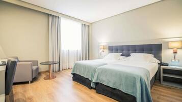 Quarto de hotel com duas camas, um espaço de estar e uma pequena mesa.