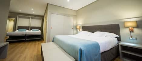 A hotel room with a large bed, a smaller bed, a desk, and a bench.