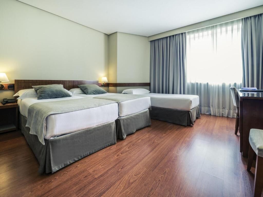 Ein Hotelzimmer mit zwei Betten, einem Schreibtisch und einem Fenster mit Vorhängen.