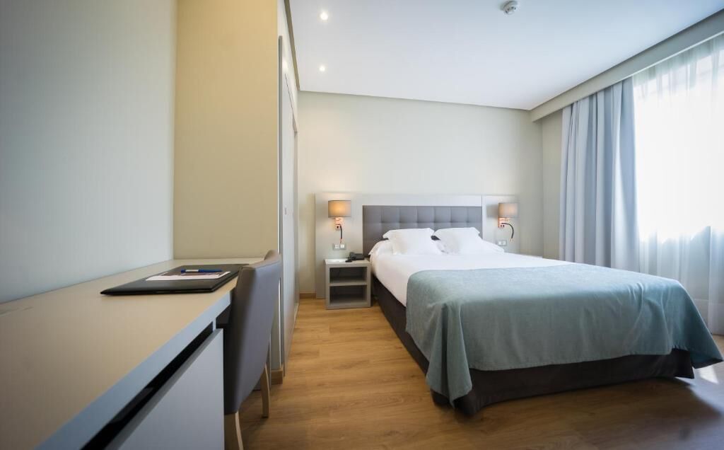 A hotel room with a bed, bedside tables, a desk, and a chair.