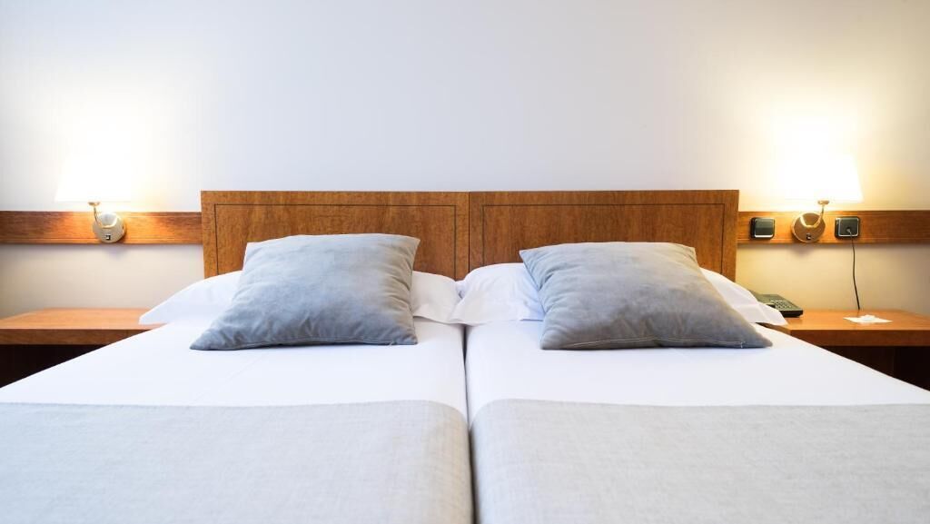 Een tweepersoonsbed met een houten hoofdbord, twee nachtkastjes en wandlampen.