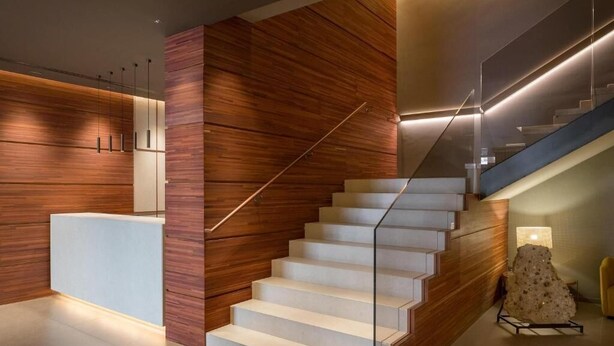 Una escalera moderna con paneles de madera y un diseño minimalista, que conduce a un espacio de recepción con mostrador.