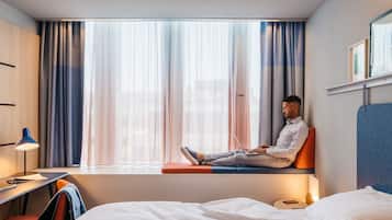 Une chambre d’hôtel avec un lit, un bureau, une chaise et une fenêtre avec des rideaux.