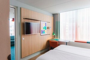 Ein Hotelzimmer mit einem Bett, einem Schreibtisch, einem Stuhl, einem Fernseher und einem Fenster mit Vorhängen.