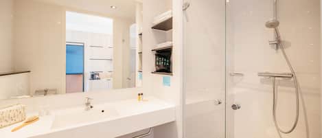 Un baño moderno con un espejo grande, un lavabo blanco y una zona de ducha con mampara de cristal.