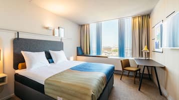 Hotellihuone, jossa on sänky, työpöytä, tuoli ja ikkuna, jossa on verhot.