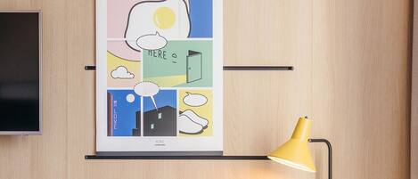 Une chambre d’hôtel moderne avec un mur lambrissé en bois, un bureau doté d’une lampe de bureau jaune, une chaise de couleur moutarde et un tableau encadré au-dessus du bureau.