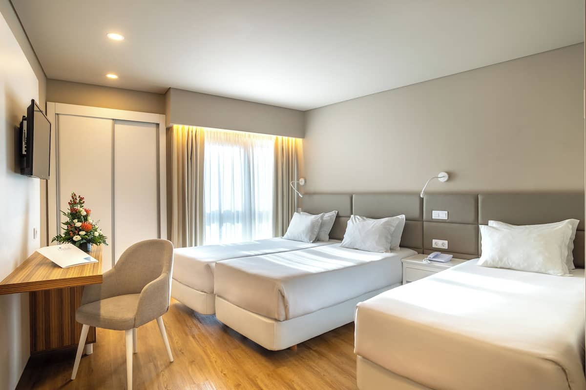 Een hotelkamer met twee bedden, een bureau, een stoel, een televisie en een raam met gordijnen.