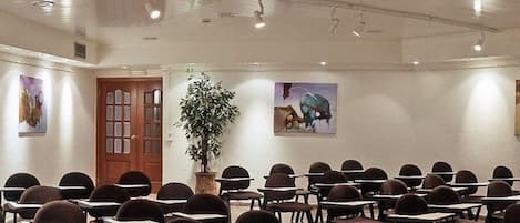 A conference room with rows of desks and chairs, a wooden door, and two wall-mounted paintings.