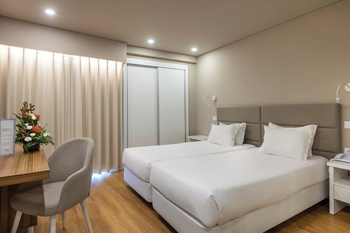 Een hotelkamer met twee bedden, een bureau, een stoel, een nachtkastje en een wandlamp.