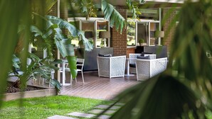 Eine Terrasse im Freien mit Korbmöbeln, einer Backsteinwand und großen Fenstern.