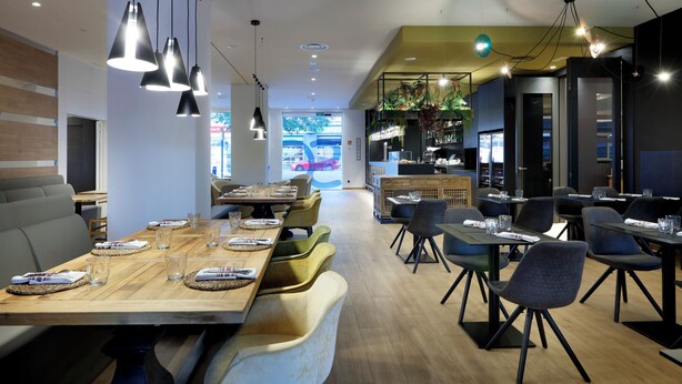 Ein modernes Restaurant mit Holztischen, schwarzen Stühlen und hängenden Pendelleuchten.