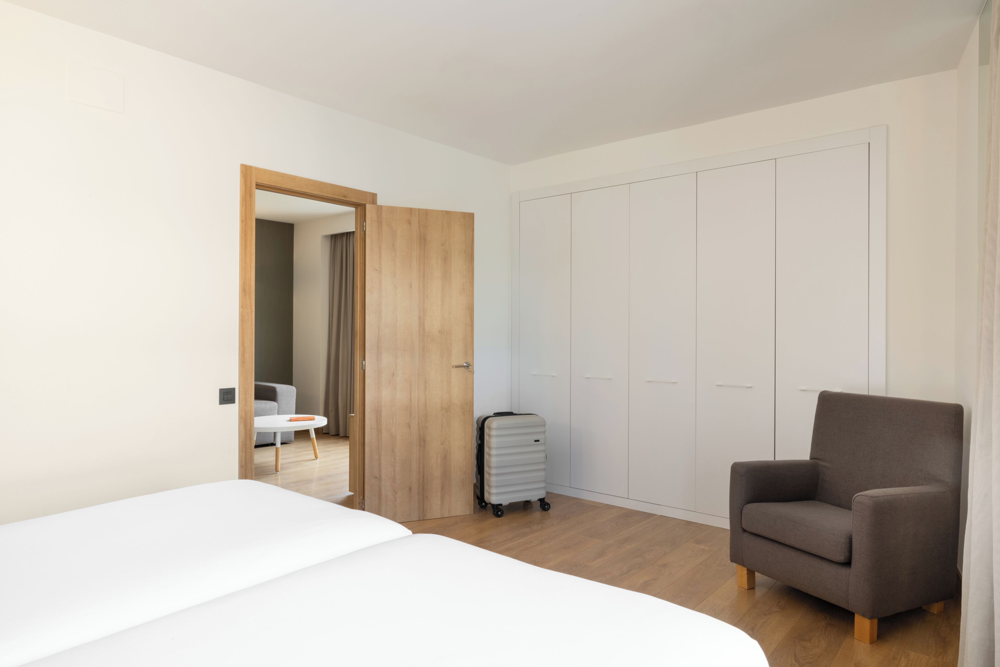 Una habitación de hotel con cama, una silla, un armario y una maleta.